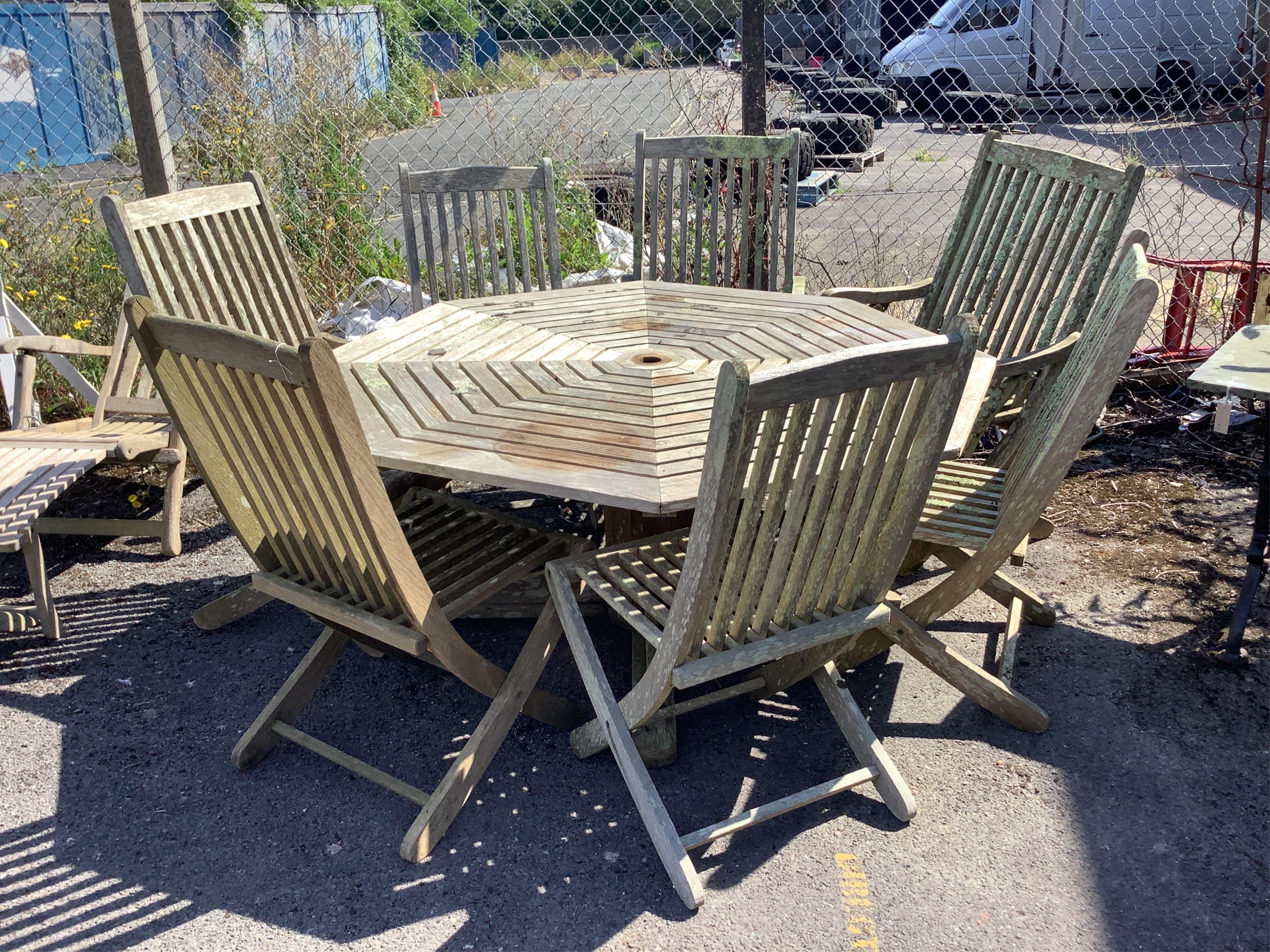 A weathered teak octagonal garden table, width 159cm, height 72cm, together with eight slatted teak folding garden chairs, four with arms. Condition - fair